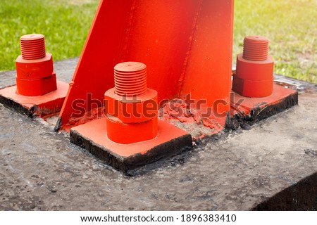 The red metal support is bolted to the concrete base with large bolts. Fixing a tower or tower to the ground. Close-up
