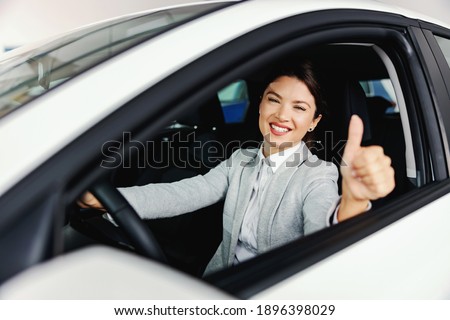 Smiling woman sitting in the car she wants to buy and sowing okay sign. Car salon interior.