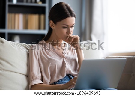 Close up thoughtful upset woman looking at laptop screen, pondering ideas or difficult tasks, sitting on couch at home, pensive young female touching chin, reading news, waiting for message Royalty-Free Stock Photo #1896409693