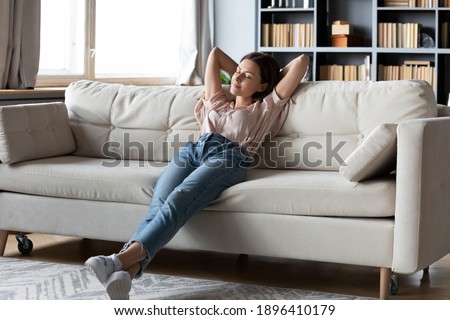 Full length calm woman with closed eyes resting on cozy couch, leaning back, enjoying lazy leisure time, attractive peaceful young female relaxing, daydreaming, taking nap on sofa at home Royalty-Free Stock Photo #1896410179
