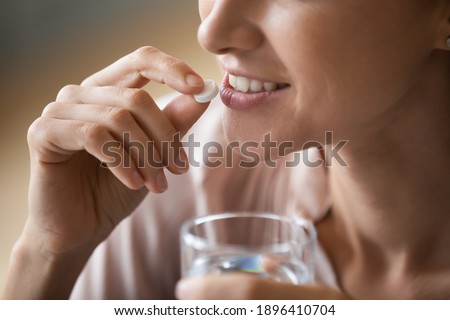 Close up smiling attractive woman holding white round pill and glass of water, happy young female taking supplement, daily vitamins for hair and skin, natural beauty, healthy lifestyle concept Royalty-Free Stock Photo #1896410704