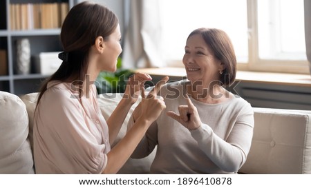 Close up smiling mature mother and grownup daughter speaking sign language, sitting on couch, young woman with elderly mum enjoying pleasant conversation, communicating, showing gestures, deaf family Royalty-Free Stock Photo #1896410878