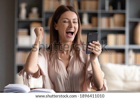 Close up overjoyed woman looking at phone screen, celebrating success, showing yes gesture, sitting at work desk, young female excited by good news in email or message, job promotion, money refund Royalty-Free Stock Photo #1896411010
