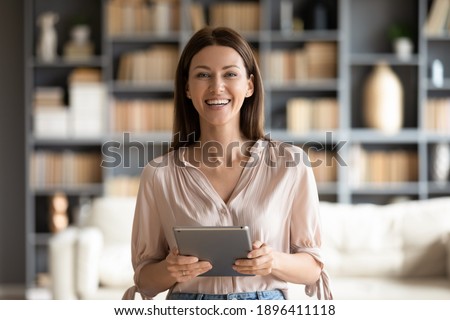 Head shot portrait smiling woman holding modern computer tablet in hands, standing at home, happy businesswoman looking at camera, female support operator ready to consulting client online