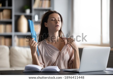 Close up thirsty woman waving paper fan, sitting at desk with laptop in room without air conditioner, exhausted tired young businesswoman suffering from heat, hot summer weather or fever Royalty-Free Stock Photo #1896411448
