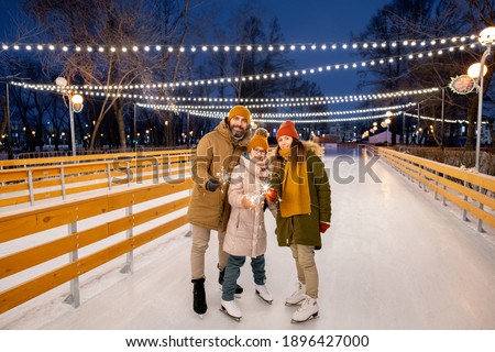 Portrait of happy family of three with sparklers standing on ice rink outdoors during Christmas holidays