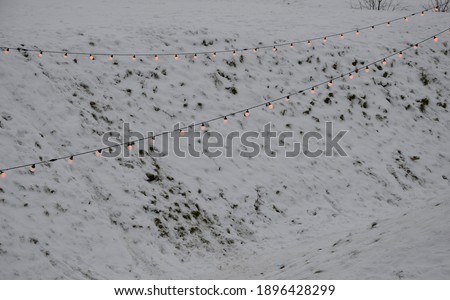 view of winter snowy slopes of a ski resort with lit chains of light bulbs. These lights are used at celebrations, weddings and party dances