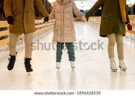 Close-up of family holding hands with child and skating on ice rink outdoors in winter