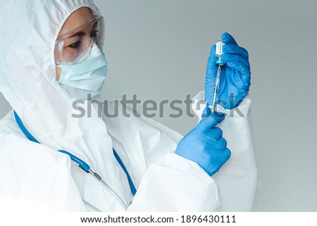 Doctor or nurse in a protective suit holds a syringe and a covid 19 vaccine