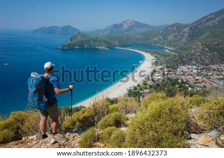 Hiking on Lycian way trail. Man with backpack enjoy view of Oludeniz beach and Blue Lagoon from Lycian Way trail, Mediterranean coast in Turkey Royalty-Free Stock Photo #1896432373