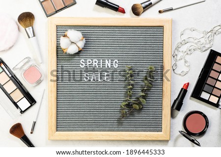 Text Spring Sale on the letter board and assortment of decorative cosmetic on white marble background top view. Spring cosmetic sale concept. Beauty shop sale banner, copy space for your text.
