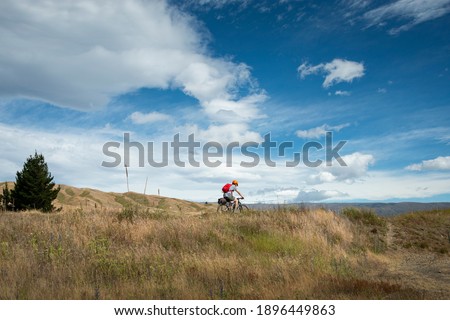 A young man cycling the Otago Central Rail Trail under the white clouds, at Chatto Creek, South Island, New Zealand
