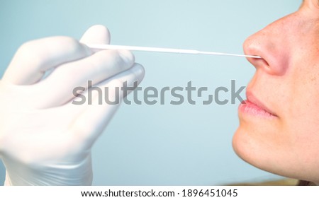 A nurse wearing latex gloves inserts a swab into a woman's nose to collect a possible positive COVID-19 sample during the pandemic. Antigen test procedure. Royalty-Free Stock Photo #1896451045