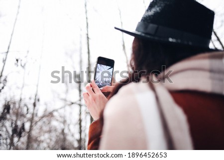 Traveler takes picture of snowy landscape in winter forest on mobile phone