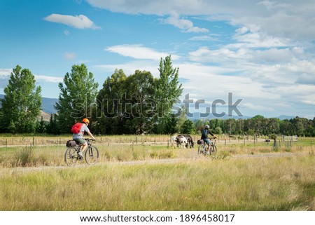Two young people cycling the Otago Central Rail Trail with horses grazing by the side of the track, South Island, New Zealand