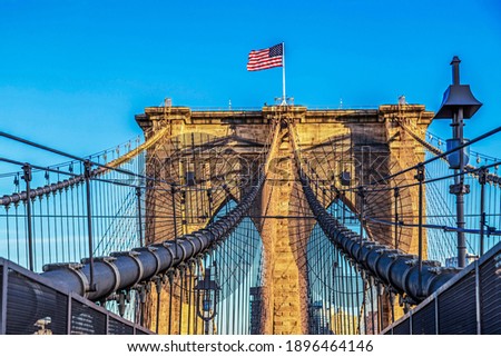 View of Brooklyn bridge structure in afternoon light with american flag. New York, USA.