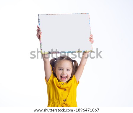 A beautiful European girl holds a white sheet of paper, a white sign on a white background and smiles.