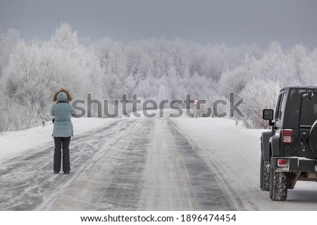 a girl takes photos of the road standing next to a black SUV