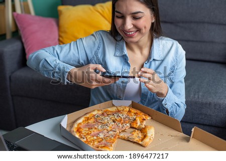 A young smiling woman is taking a picture of pizza at home.