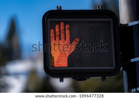 A red hand sign tells pedestrians not to cross a busy street.