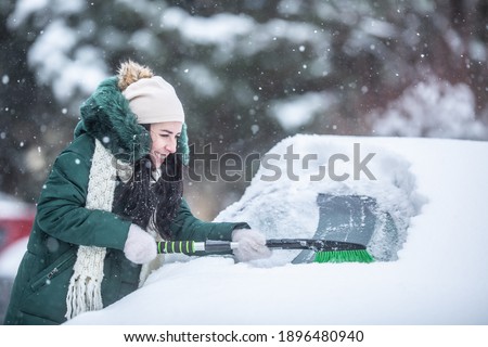 Woman struggles to scrape ice and snow off the snowed-in car on a parking lot.
