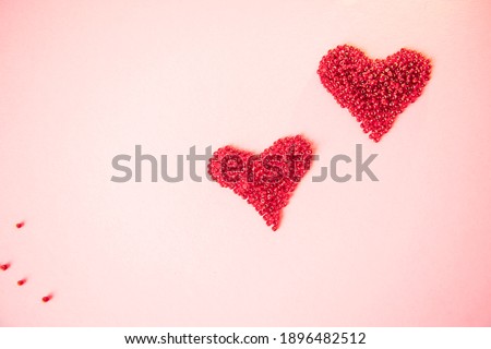 Two rred hearts made of beads as a symbol of love on an isolated pastel light pink background. Greeting card for Valentine's Day, Mother's Day or other holiday. Selective focus. Flat lay. Copy space.