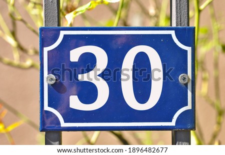 A blue house number plaque, showing the number thirty (30)  