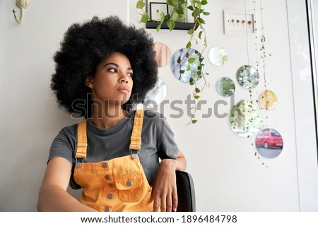 Young thoughtful pensive stylish African American gen z female hipster woman with afro hair looking through window thinking reflecting sitting lost in thoughts at home, in modern cafe alone indoors. Royalty-Free Stock Photo #1896484798