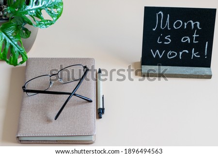 Home work place with time diary, pen, eyes glasses and black blank with inscription  Mom is at work. Home remote working concept.