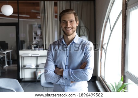 Head shot portrait smiling successful young businessman standing with arms crossed in modern office, happy executive boss startup founder looking at camera, posing for corporate photo alone Royalty-Free Stock Photo #1896499582