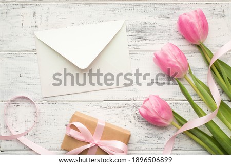 Happy mom's day concept. Overhead flat lay close up view photo picture of three pastel color flowers with wrapped kraft present sulky ribbon and open white envelope on wooden table