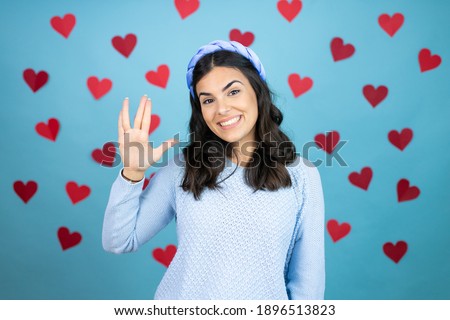 Young beautiful woman over blue background with red hearts doing hand symbol