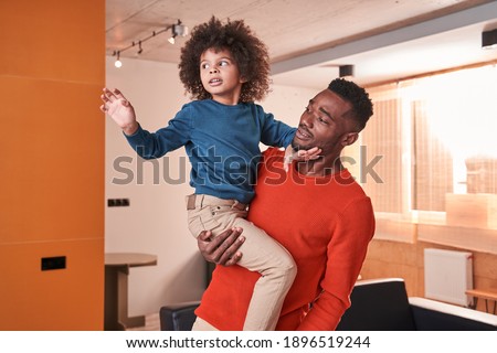 Best friends. Calm multiracial father holding at the hands his little curly son and speaking with him at the living room. Happy childhood concept. Stock photo