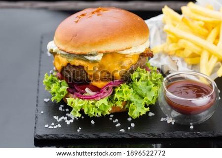 pork burger with ketchup and french fries. wooden board on black background	