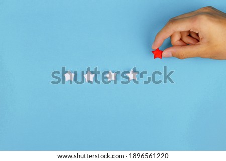 Hand put paper red star in whie row on blue background. Giving review, Sale rating and customer satisfaction concept. Royalty-Free Stock Photo #1896561220