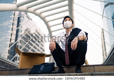 Asian business man feeling sad after unemployment from his company. The man sitting outdoor feeling stress worry about losing the job due to world economic problem from covid 19 crisis concept. Royalty-Free Stock Photo #1896595480