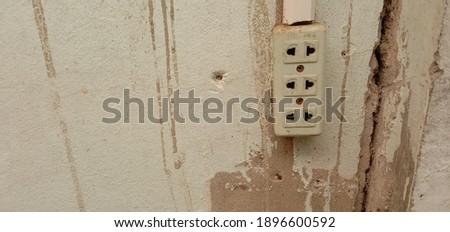Three-eyed plug attached to an old cement wall, cracked.
