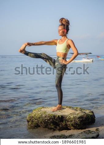 Young woman practicing Utthita Hasta Padangusthasana, Standing Big Toe Hold. Work out on the beach. Strong body. Yoga retreat. Balance and concentration. Thomas beach, Bali, Indonesia