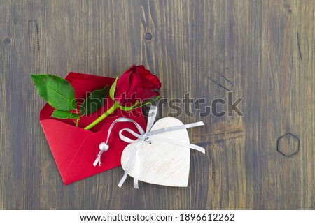 Red rose in envelope and heart medallion on wooden background with free copy space. Wishes, greetings and love message