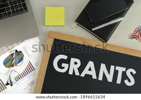 Black chalkboard with business accessories (notepad, smartphone, diary, fountain pen, glasses and calculator) and text Grants. Top view. Royalty-Free Stock Photo #1896615634