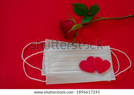 Aerial view of two surgical masks with two red hearts and red rose on red background. Valentine's Day concept and new normal for COVID-19. Horizontal photography and copy space.