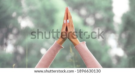 Close-up of hands joined together in a namaste gesture against a backdrop of nature. Mental health and wellbeing concept. Banner size.