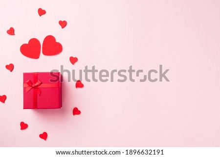 Valentines' day background. Red gift box with ribbon bow and wood red hearts shaped composition greeting card for love isolated on pink background with copy space. Top View from above