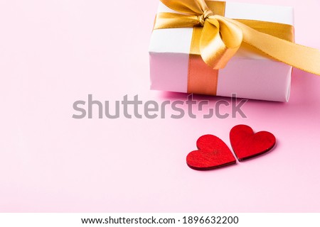 Valentines' day background concept. White gift box with a golden bow ribbon and wood red hearts composition greeting card for happy love isolated on pink background with copy space. View from above