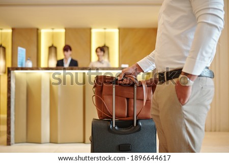 Cropped image of hotel guest standing in lobby with luggage after checking in Royalty-Free Stock Photo #1896644617