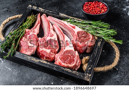 Raw lamb meat chops steaks in a wooden tray. Black background. Top view. Royalty-Free Stock Photo #1896648697