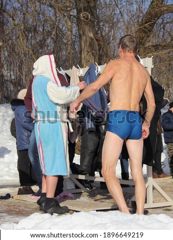 Winter ice swimming sport, a Russian people changing clothes, man in a swimming trunks and men in bathrobe at Sunny frosty winter day, healthy lifestyle
