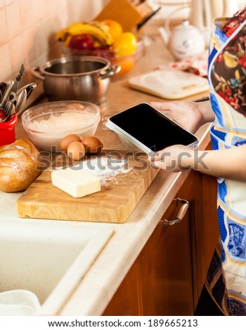 Closeup photo of woman looking recipe on tablet while making dough