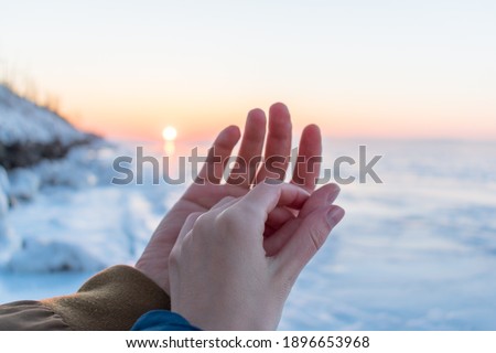 Hands of a man and a woman together on the background of the sunset and winter sea