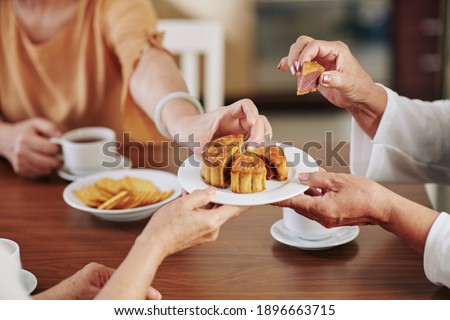 Hands of senior women eating delicious traditional moon cake when celebrating mid autumn festival at home Royalty-Free Stock Photo #1896663715
